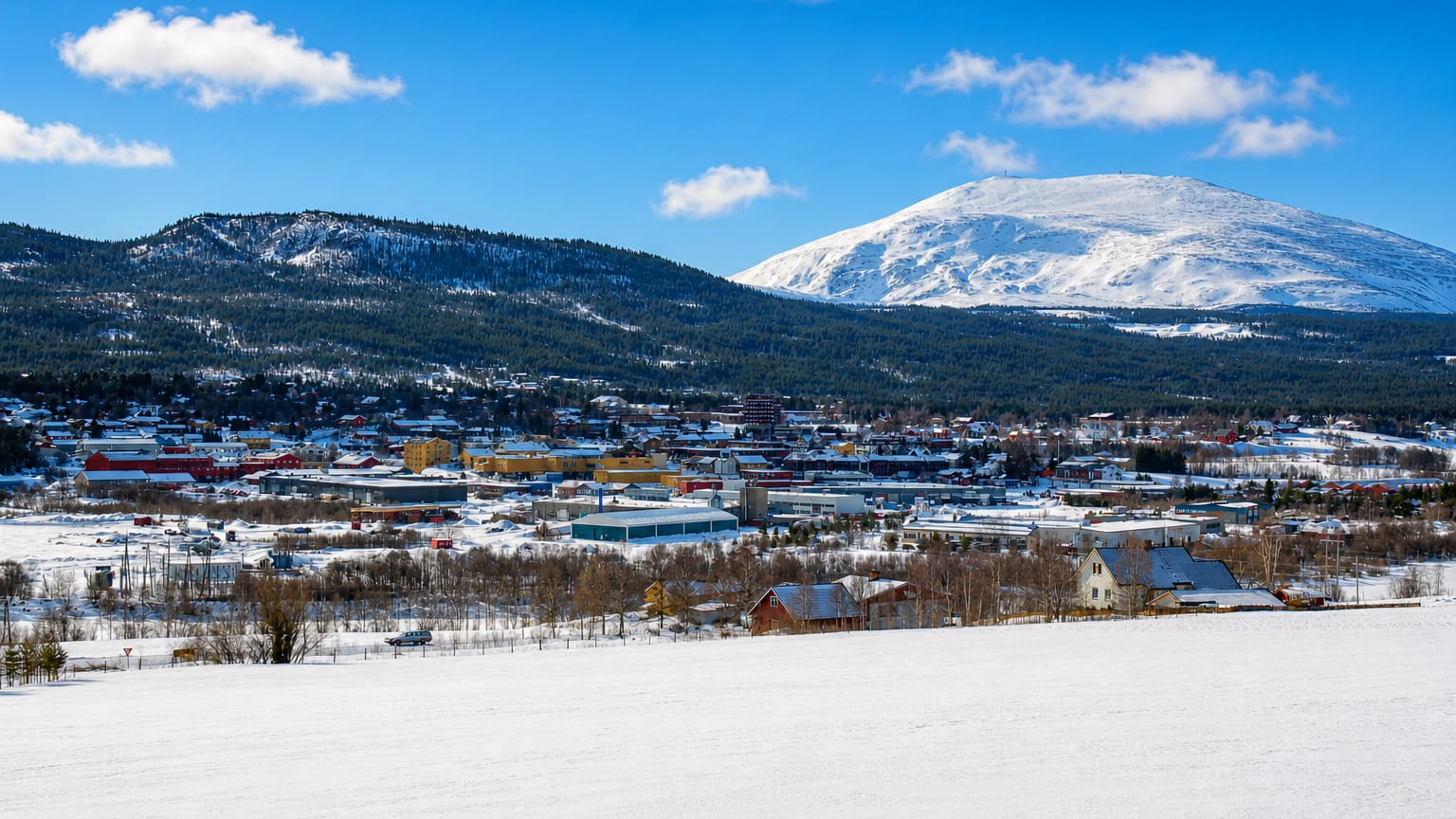 Winter view of Tynset, Norway, spread below a snow-capped mountain under a clear blue sky