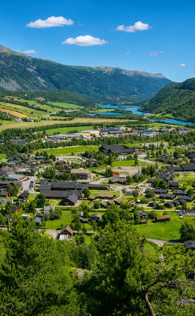 Elevated view of Vagamo village on the green valley floor of Gudbrandsdalen, with the Otta river winding past forested fells in Norway.