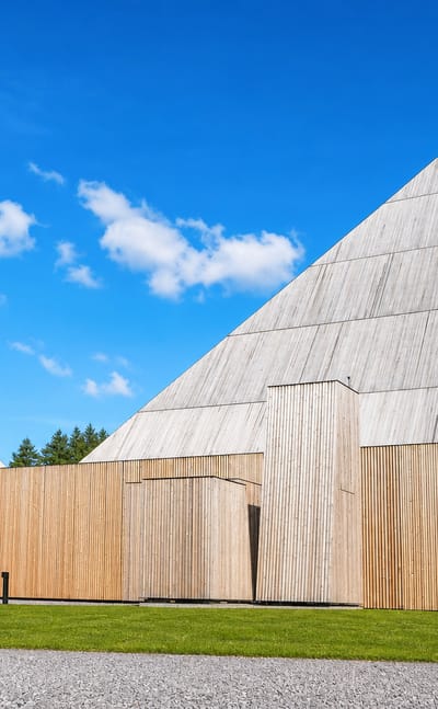 Våler's contemporary timber church with two soaring angular peaks clad in pale wood against a bright blue sky.