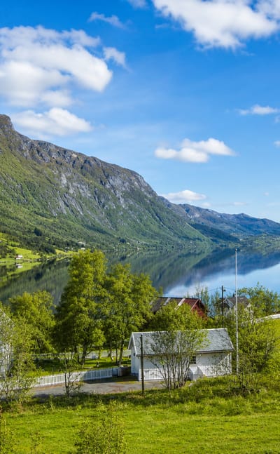 White wooden church beside a calm lake ringed by forested mountains in Vang, Norway.