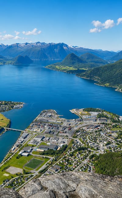 Aerial of Andalsnes on the Rauma river delta where it meets Romsdalsfjord, ringed by jagged snow-capped peaks