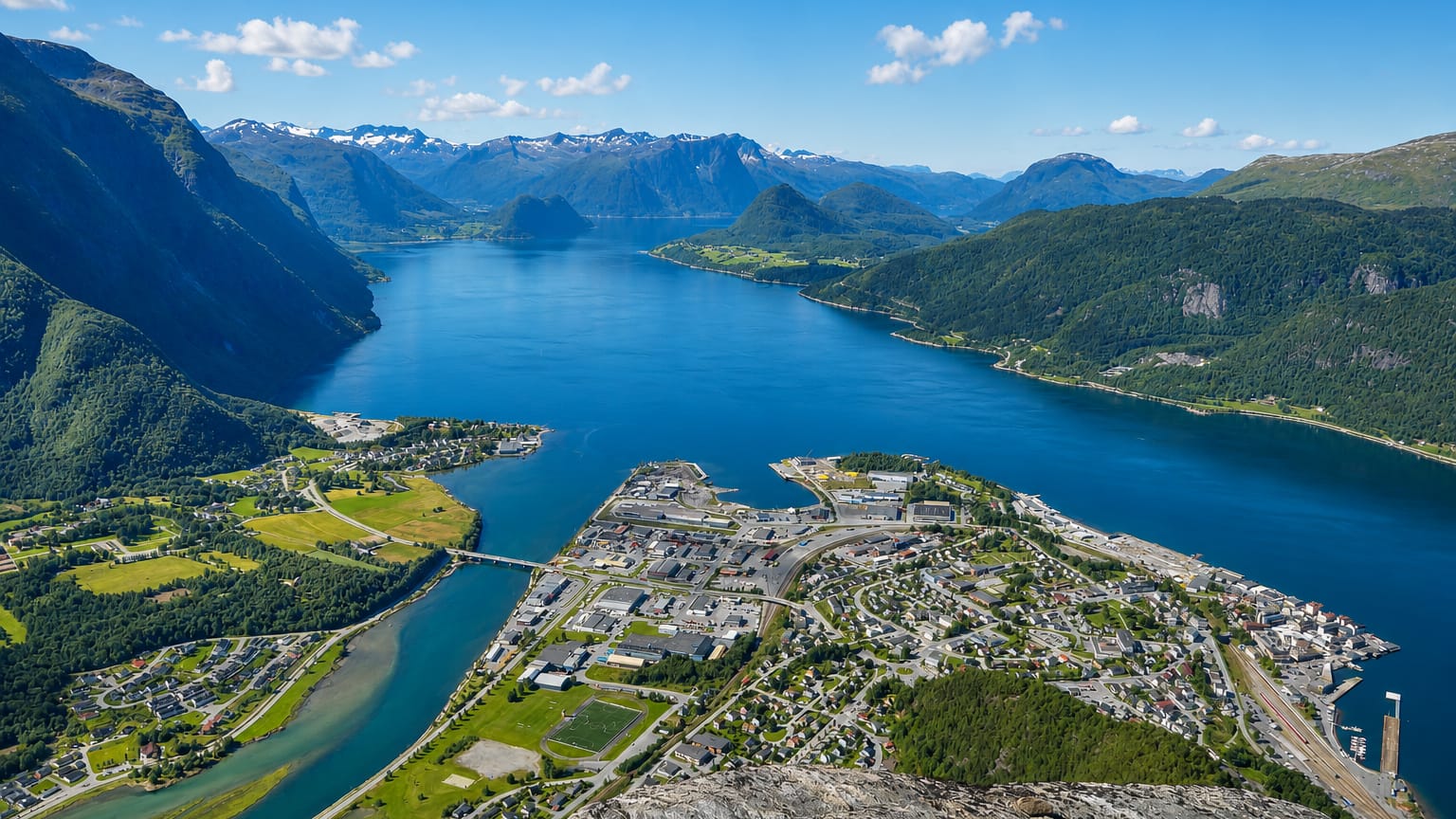 Aerial of Andalsnes on the Rauma river delta where it meets Romsdalsfjord, ringed by jagged snow-capped peaks