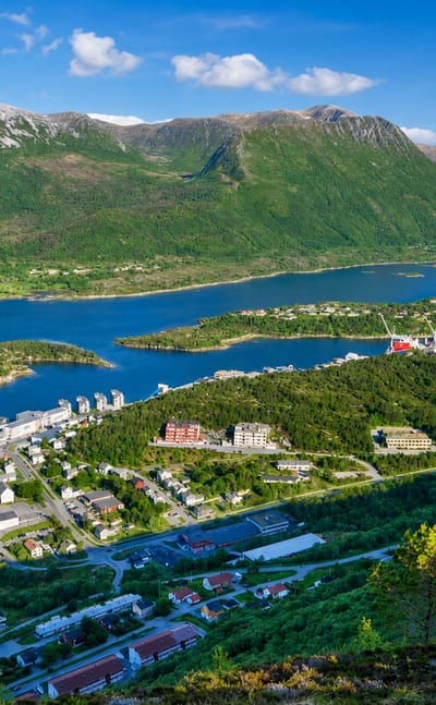 Aerial of Brattvag's fjord-side town and harbor with apartment blocks beneath green mountains, More og Romsdal, Norway