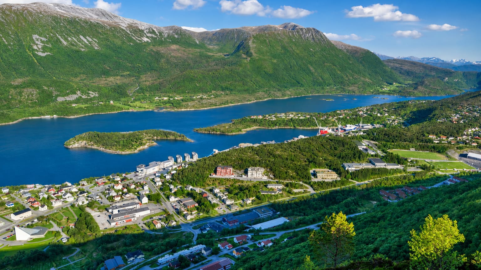 Aerial of Brattvag's fjord-side town and harbor with apartment blocks beneath green mountains, More og Romsdal, Norway