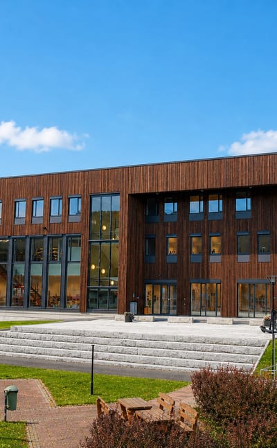 A modern timber-clad municipal building with a plaza and steps in Bruhagen, Norway.