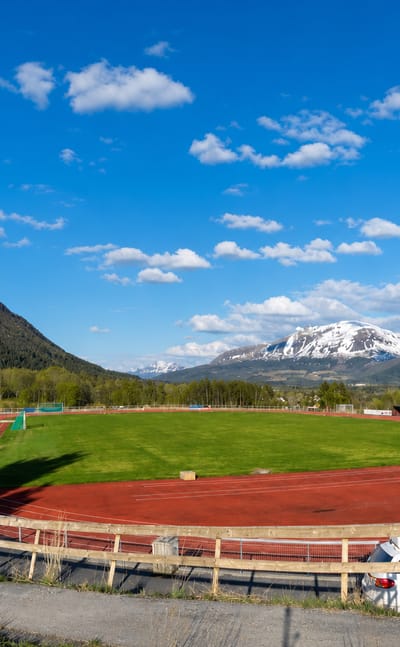 Athletics track and football pitch below snow-capped mountains on the edge of Elnesvågen, Norway.
