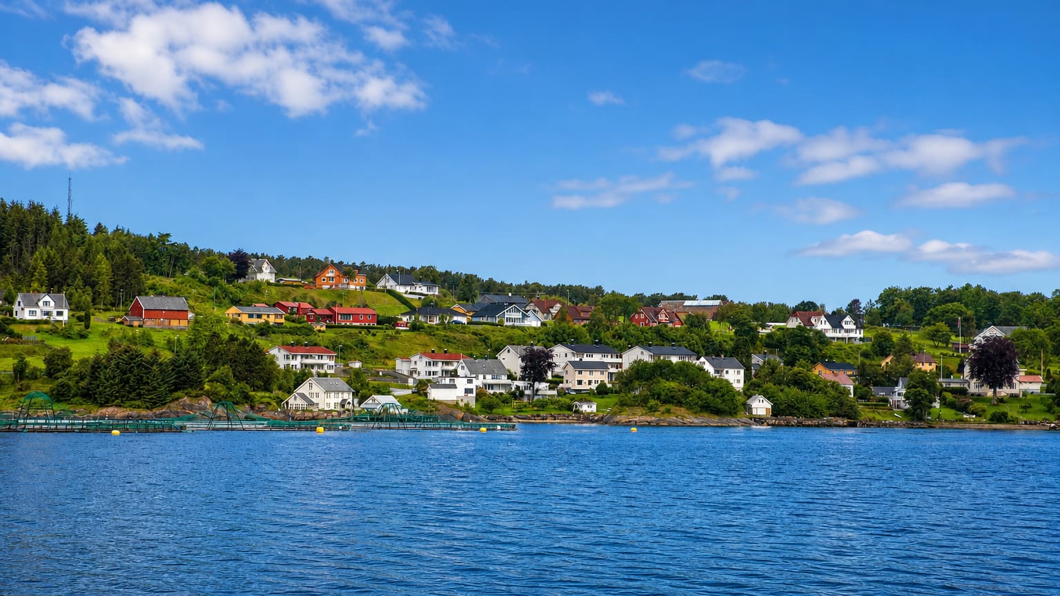 Waterfront village of Falkhytta, Norway, white and red houses on a green hillside above a calm blue fjord.