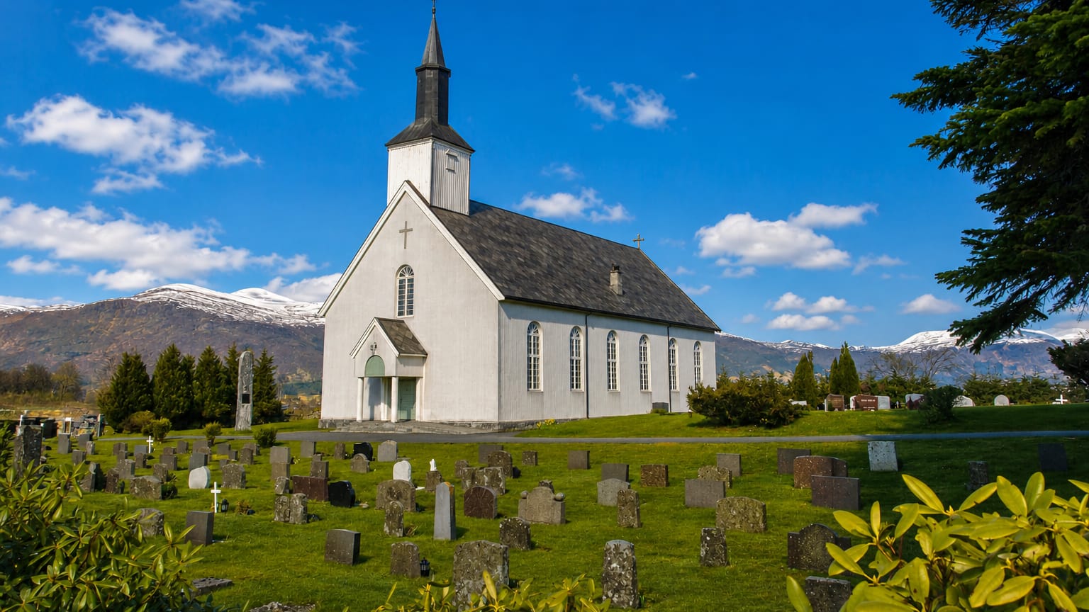 White wooden church and graveyard below snow-capped mountains at Fiska