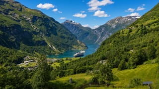 Geirangerfjord in Norway with a cruise ship on the turquoise water framed by steep green mountains and the village of Geiranger.