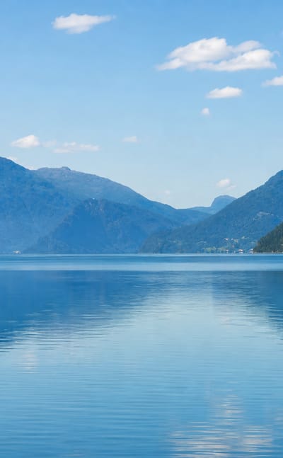 Calm blue lake mirroring forested mountains under a clear sky at Hornindal, Norway