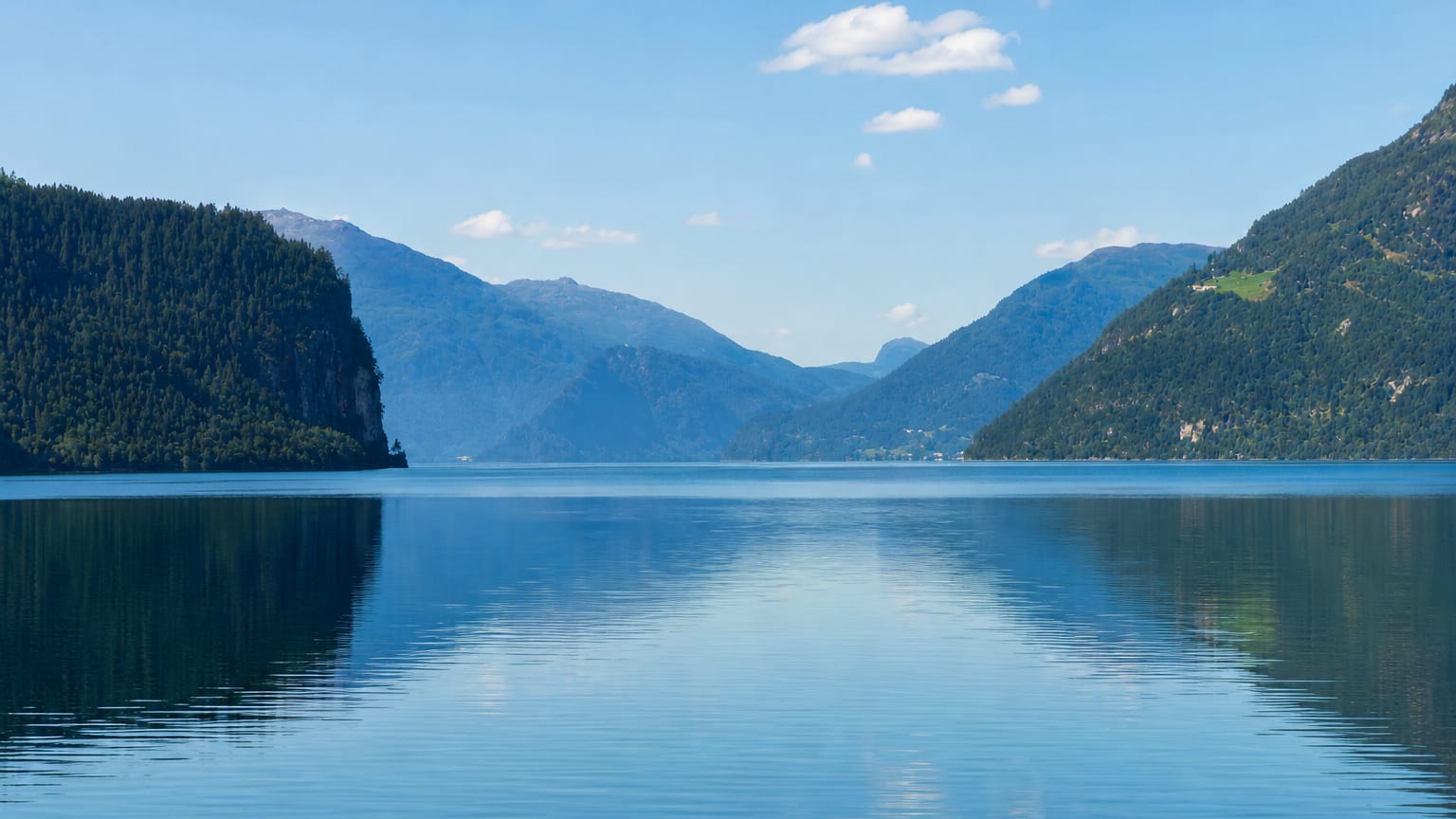 Calm blue lake mirroring forested mountains under a clear sky at Hornindal, Norway
