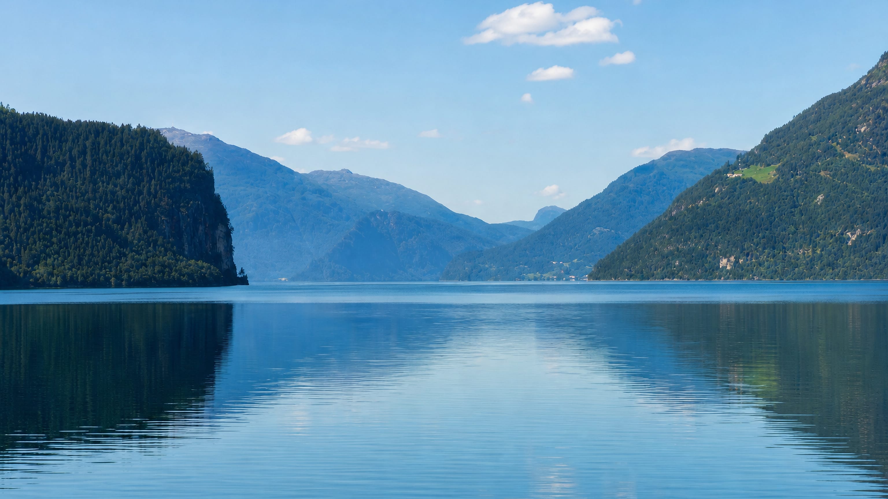 Calm blue lake mirroring forested mountains under a clear sky at Hornindal, Norway