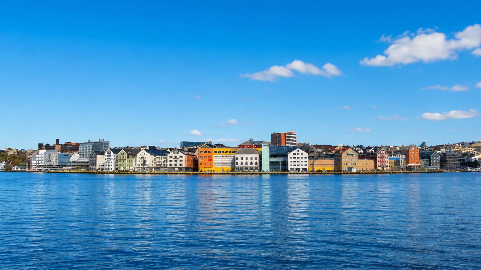 Row of colourful waterfront buildings lining Kristiansund's harbour across calm blue water