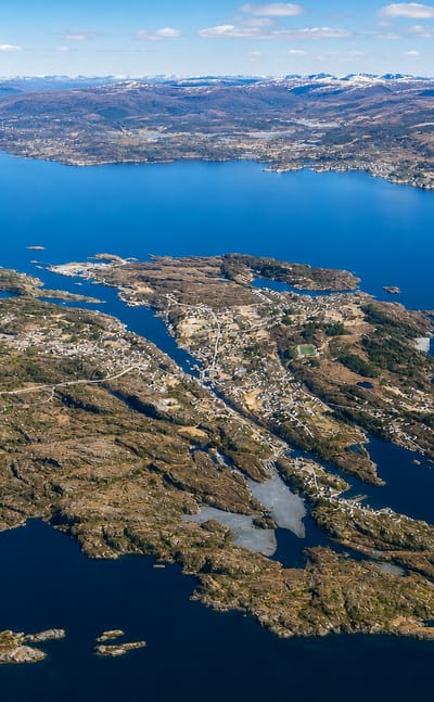 Aerial view of the island settlement of Langevag amid coastal islets with snow-capped peaks beyond, Norway