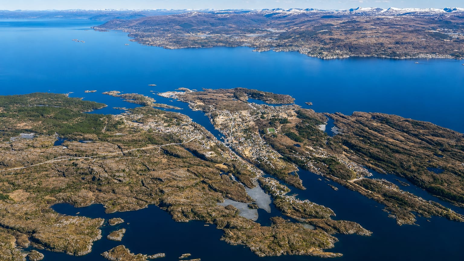 Aerial view of the island settlement of Langevag amid coastal islets with snow-capped peaks beyond, Norway