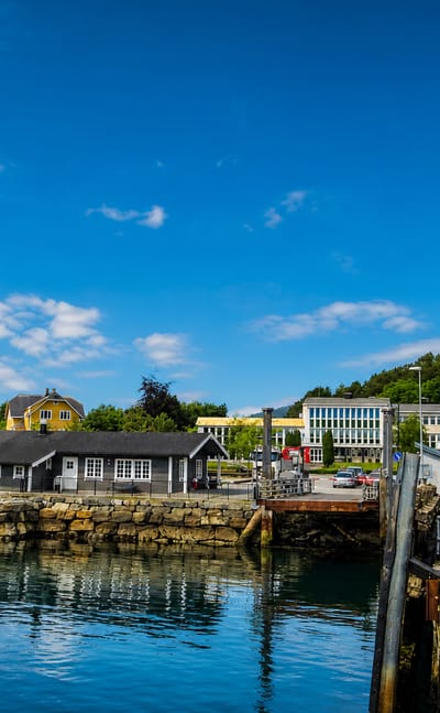 Larsnes harbour on a clear summer day, with a stone quay, waterfront houses and forested hills beside calm blue water.