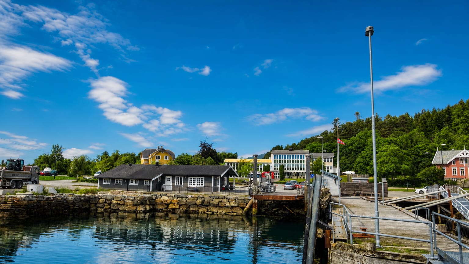 Larsnes harbour on a clear summer day, with a stone quay, waterfront houses and forested hills beside calm blue water.