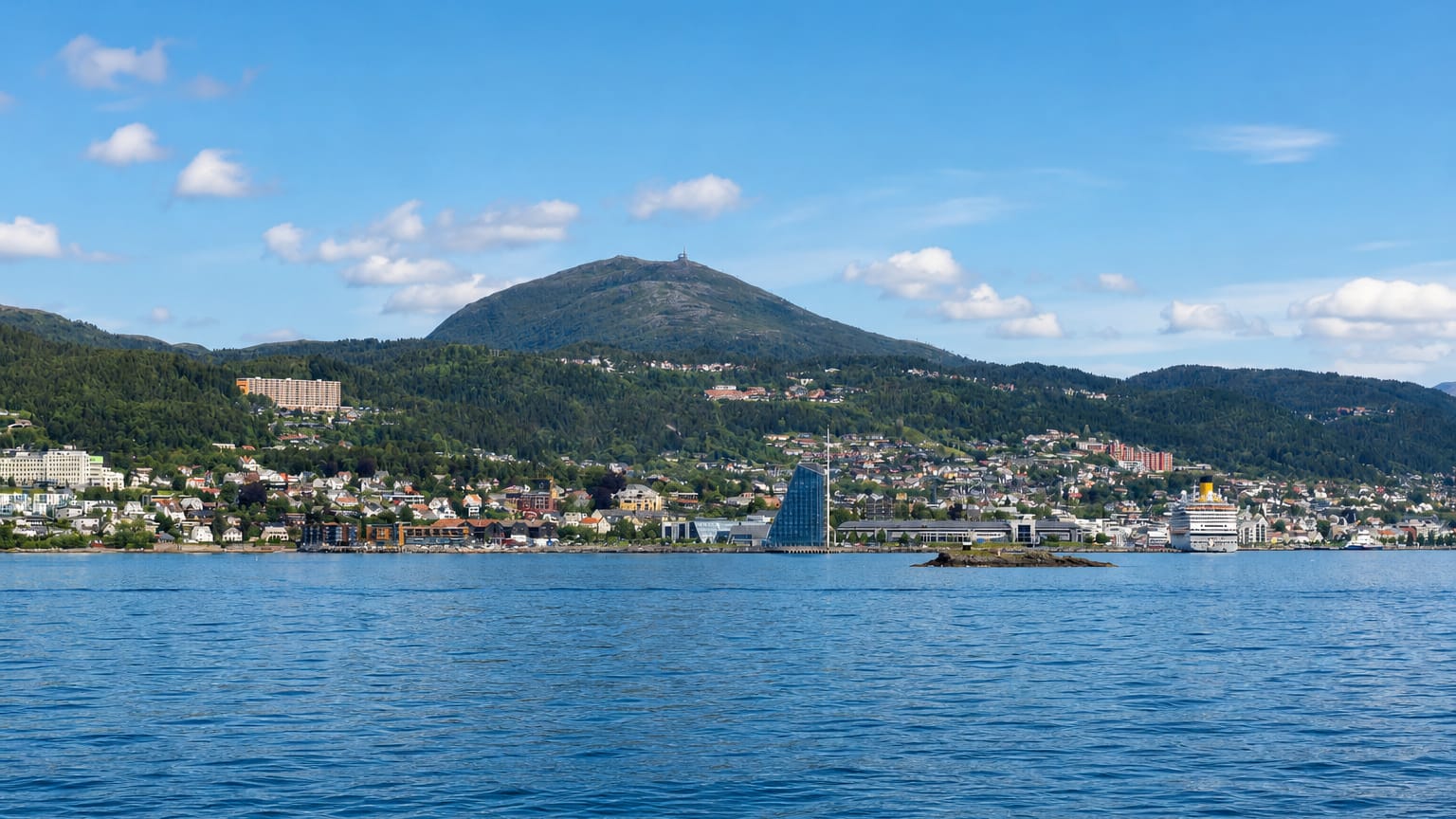Molde's waterfront beneath a forested mountain across the Romsdalsfjord with a cruise ship at the pier