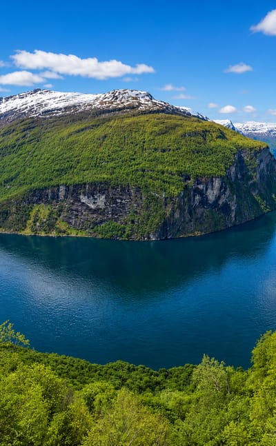 Snow-capped mountains rising above a deep blue fjord in the Stranda district of Norway