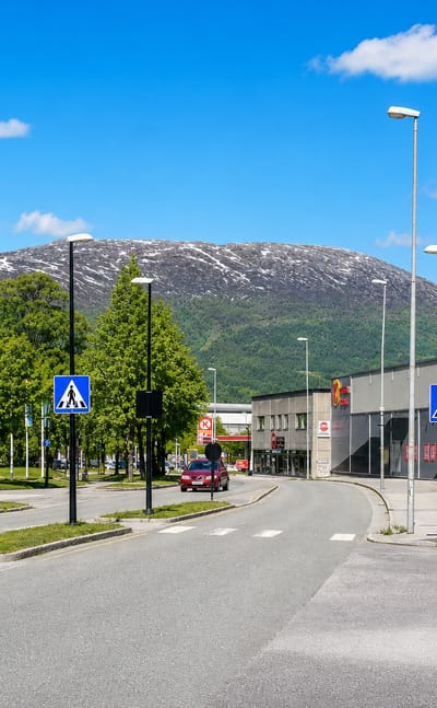 Street and roundabout with commercial buildings below a snow-streaked mountain in Sunndalsora, Norway