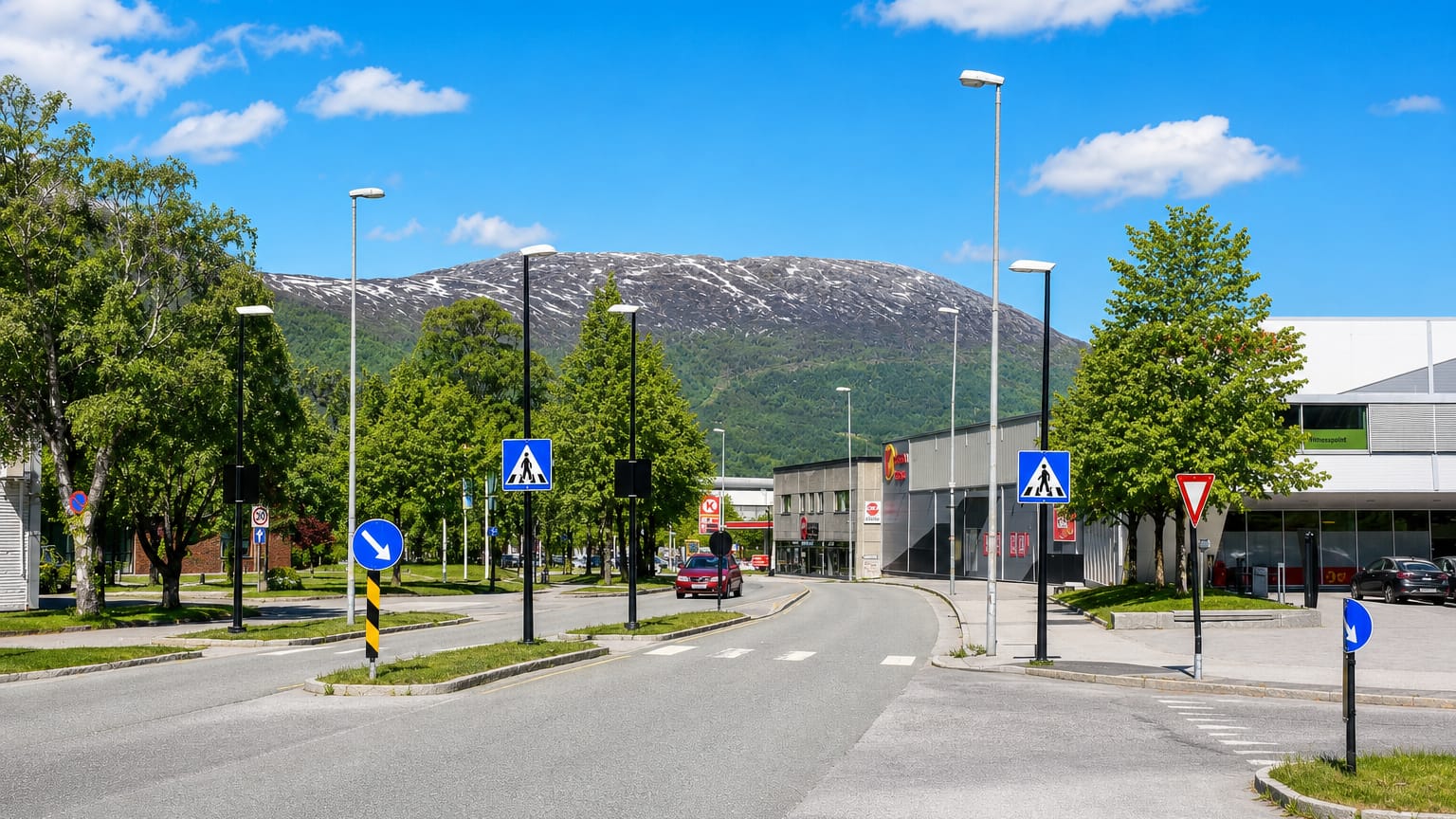 Street and roundabout with commercial buildings below a snow-streaked mountain in Sunndalsora, Norway