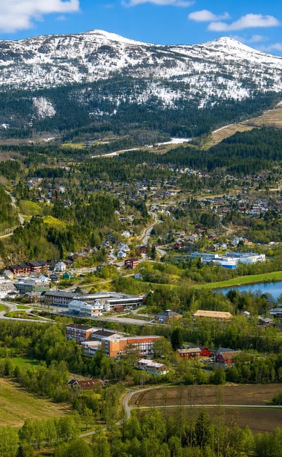 Surnadal town spread along a river through a green valley below snow-capped mountains, framed by forest and farmland.