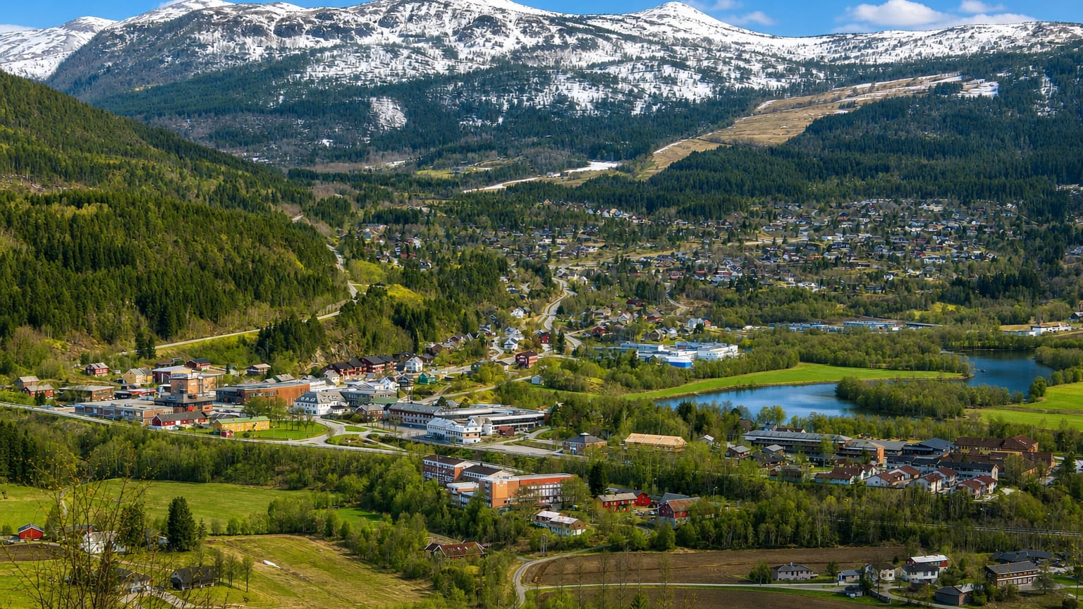 Surnadal town spread along a river through a green valley below snow-capped mountains, framed by forest and farmland.