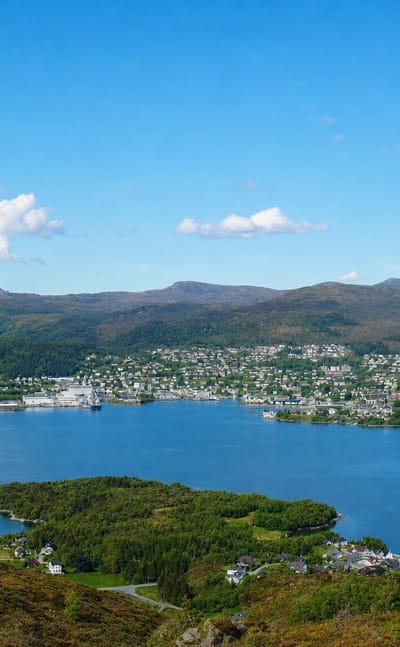 Elevated view over Ulsteinvik, Norway, spread along the blue fjord with islands and forested mountains behind.