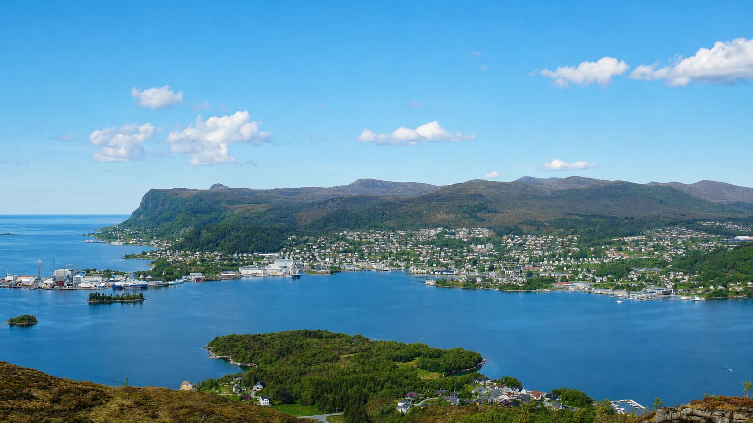 Elevated view over Ulsteinvik, Norway, spread along the blue fjord with islands and forested mountains behind.