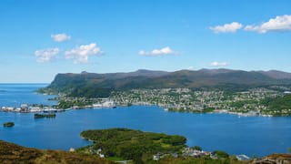 Elevated view over Ulsteinvik, Norway, spread along the blue fjord with islands and forested mountains behind.