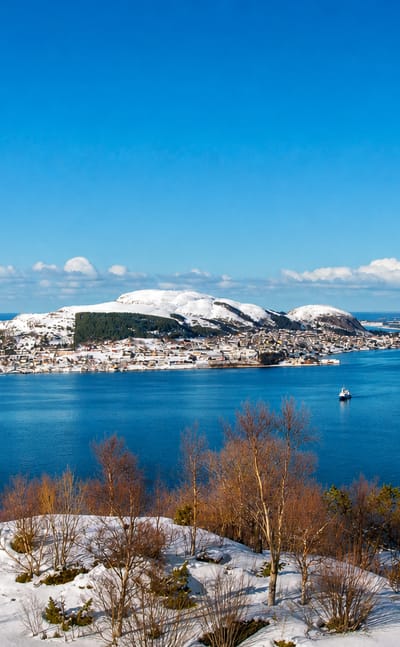 Snowy island town of Valderøy spread along the shore below a rounded hill, seen across a blue fjord, Møre og Romsdal, Norway