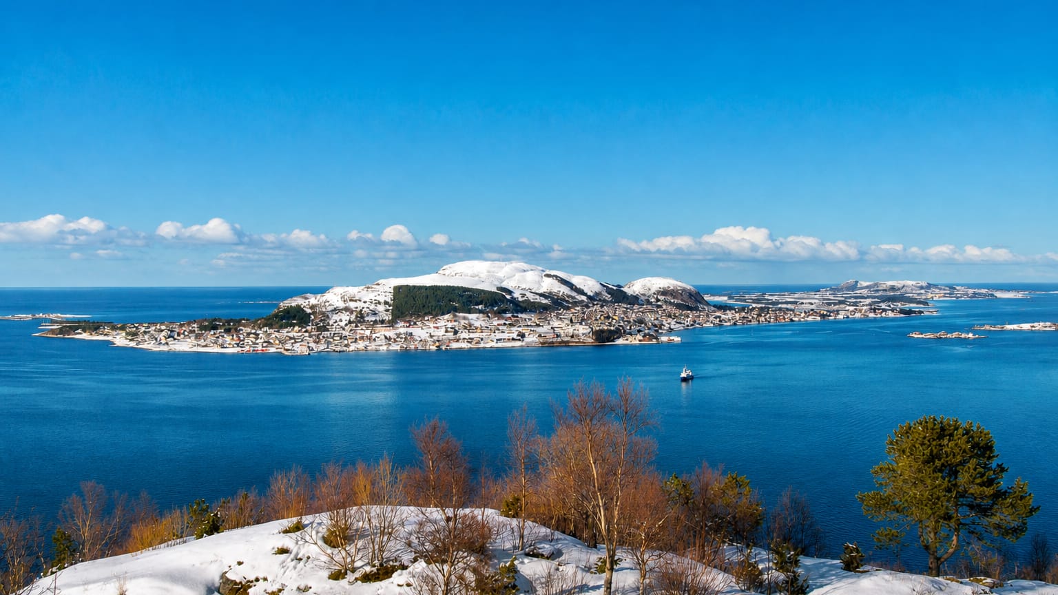Snowy island town of Valderøy spread along the shore below a rounded hill, seen across a blue fjord, Møre og Romsdal, Norway