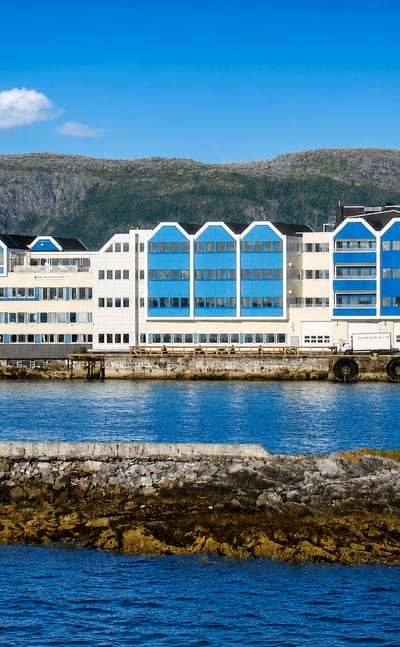 Waterfront row of white and blue gabled quayside buildings at Bronnoysund backed by low Nordland mountains