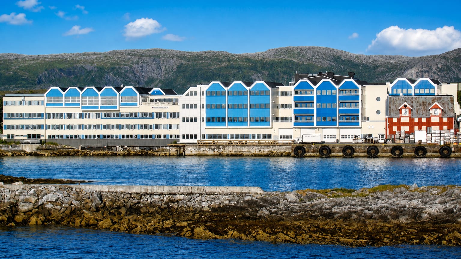 Waterfront row of white and blue gabled quayside buildings at Bronnoysund backed by low Nordland mountains