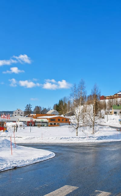 Snow-lined main street through Hattfjelldal village, Nordland, Norway, with low buildings and forested hills