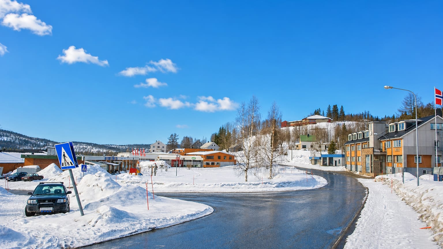Snow-lined main street through Hattfjelldal village, Nordland, Norway, with low buildings and forested hills