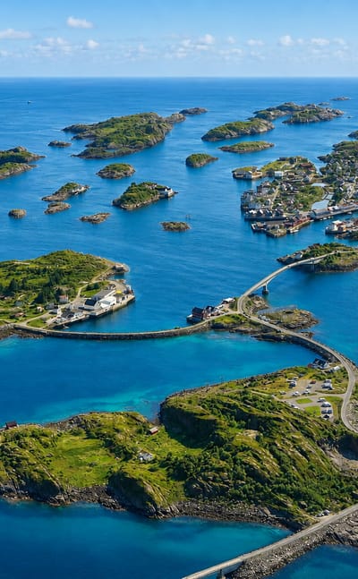 Aerial view of Henningsvaer fishing village spread across small islets linked by bridges in Norway's Lofoten islands under a clear sky.
