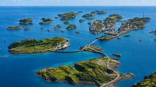 Aerial view of Henningsvaer fishing village spread across small islets linked by bridges in Norway's Lofoten islands under a clear sky.