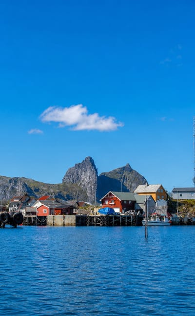 Colourful fishing houses on stilts before dramatic pointed peaks on Husøya island, Nordland, Norway