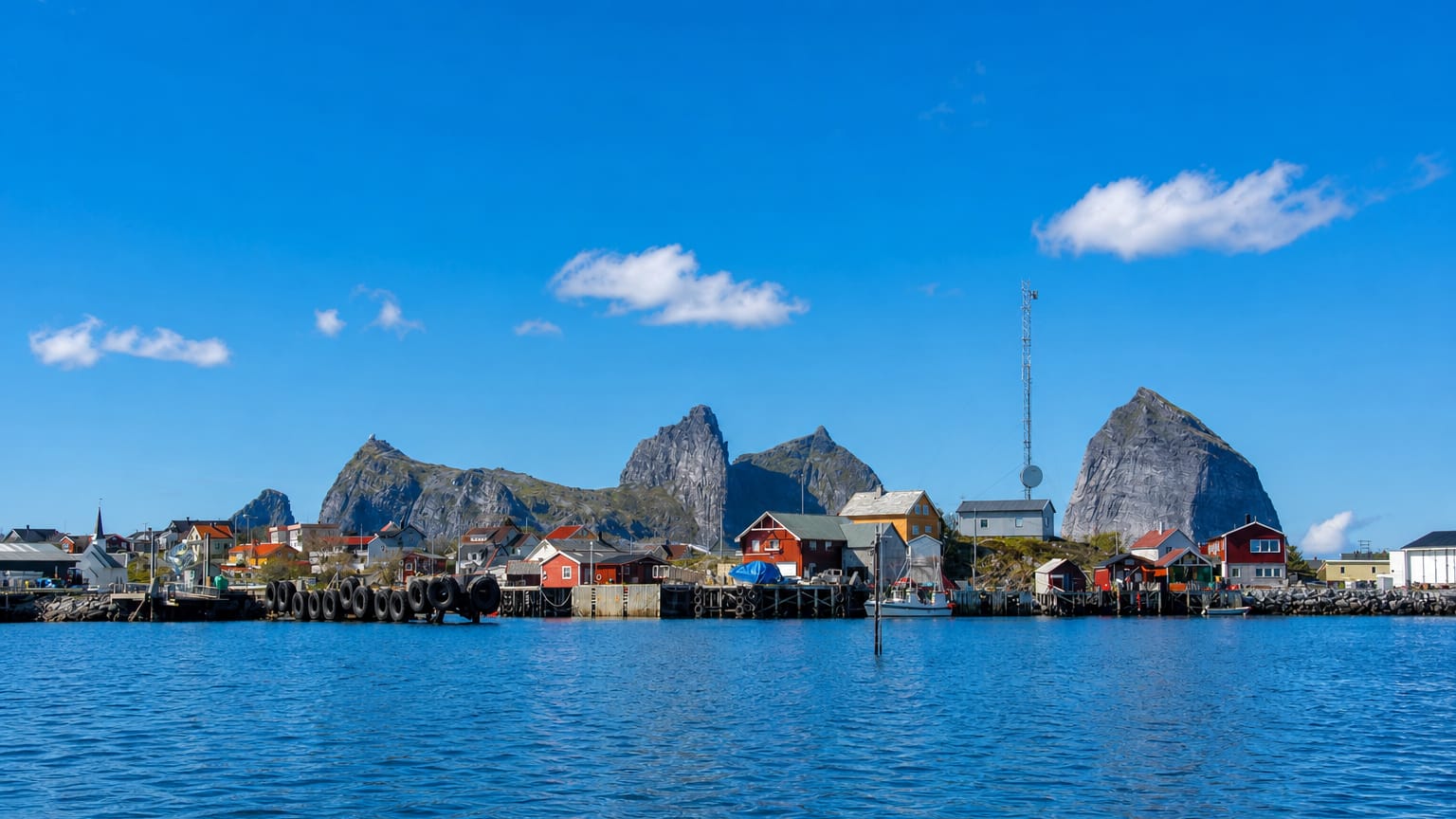 Colourful fishing houses on stilts before dramatic pointed peaks on Husøya island, Nordland, Norway