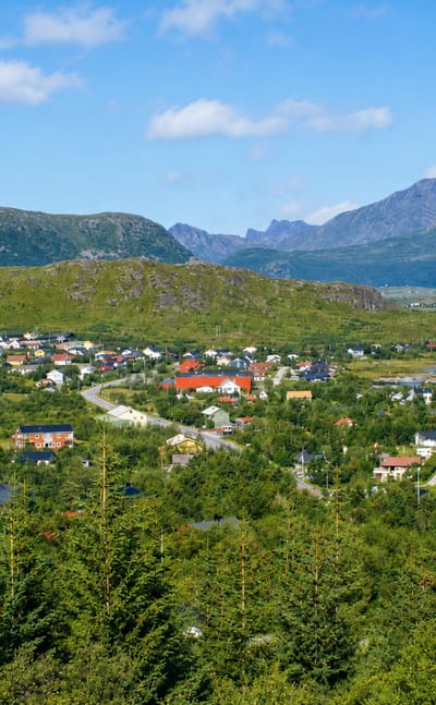 Leknes townscape spread beneath jagged Lofoten mountain peaks in Nordland on a clear summer day