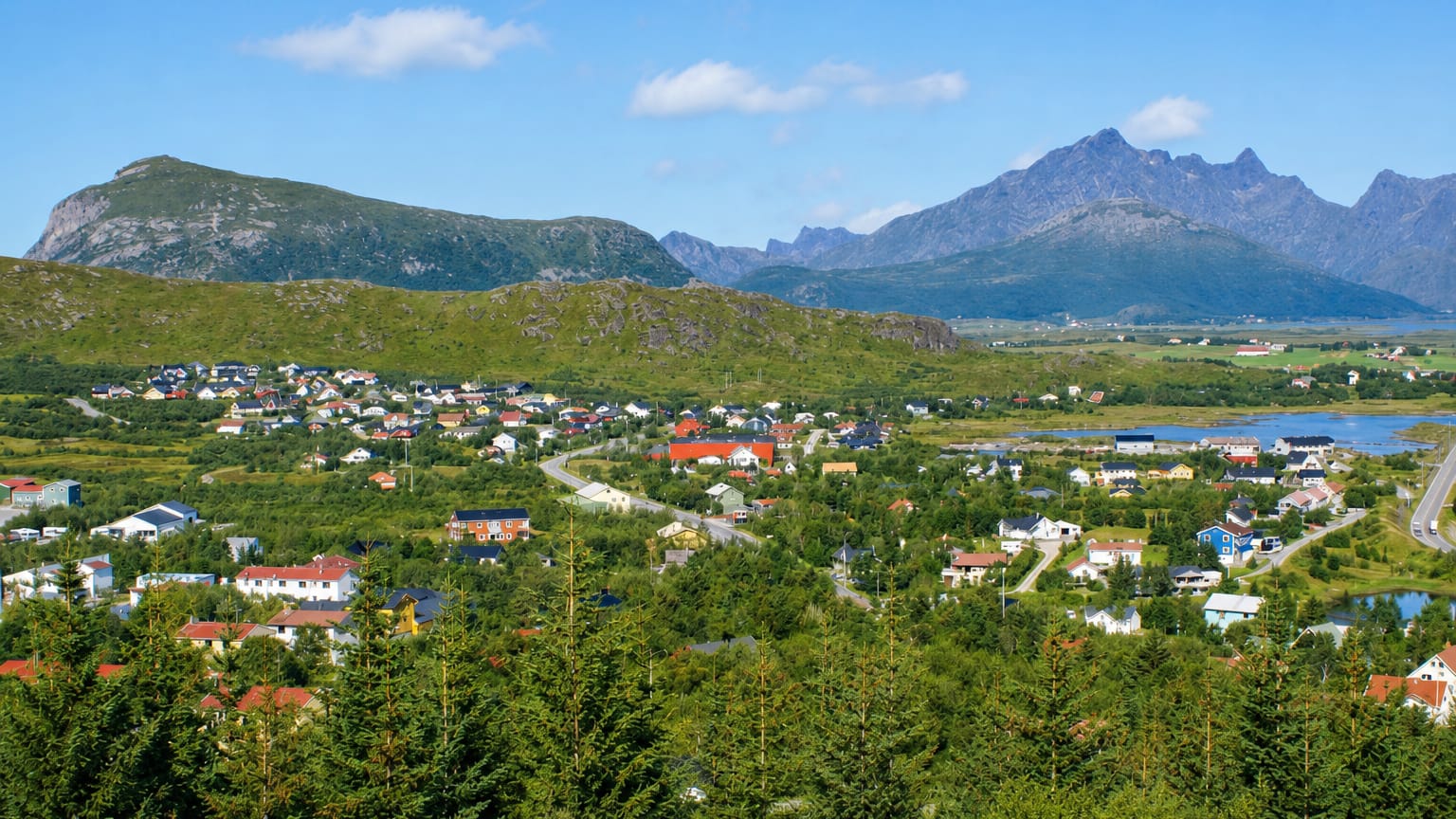 Leknes townscape spread beneath jagged Lofoten mountain peaks in Nordland on a clear summer day