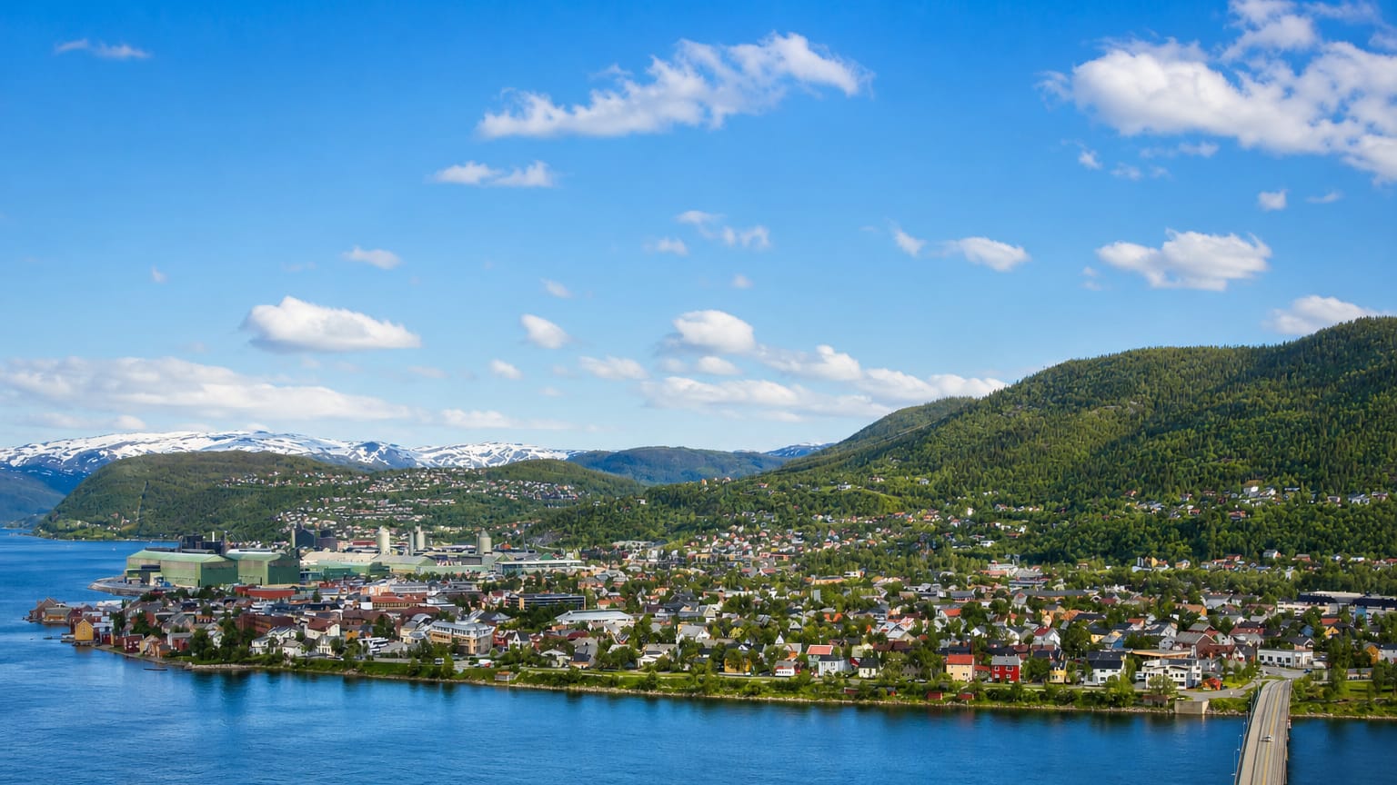 Mosjøen spread along its fjord with a waterside industrial plant, a road bridge and snow-capped mountains beyond