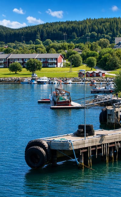 Nesna harbour with moored sailboats and fishing boats, a quay, and the white hillside church above forested Helgeland hills.