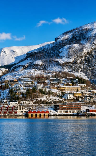 Colourful houses on a snow-covered hillside beneath a fjord peak at the waterfront of Ornes in Nordland, Norway.