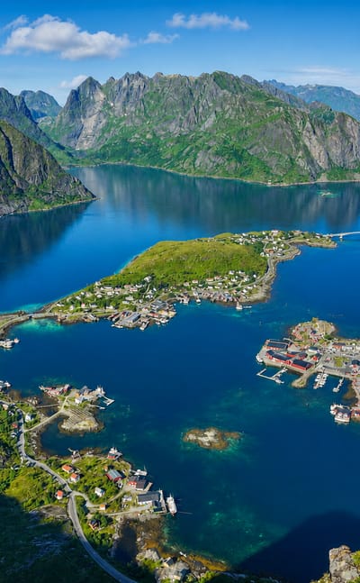 Aerial view of Reine, Norway, its village spread across islands in a blue Lofoten fjord beneath jagged peaks