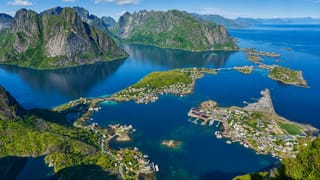 Aerial view of Reine, Norway, its village spread across islands in a blue Lofoten fjord beneath jagged peaks