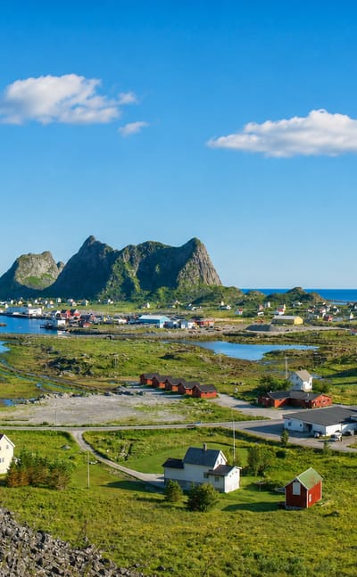 Sorland village on Vaeroy, Norway, with houses and harbour below a jagged Lofoten peak beside the sea