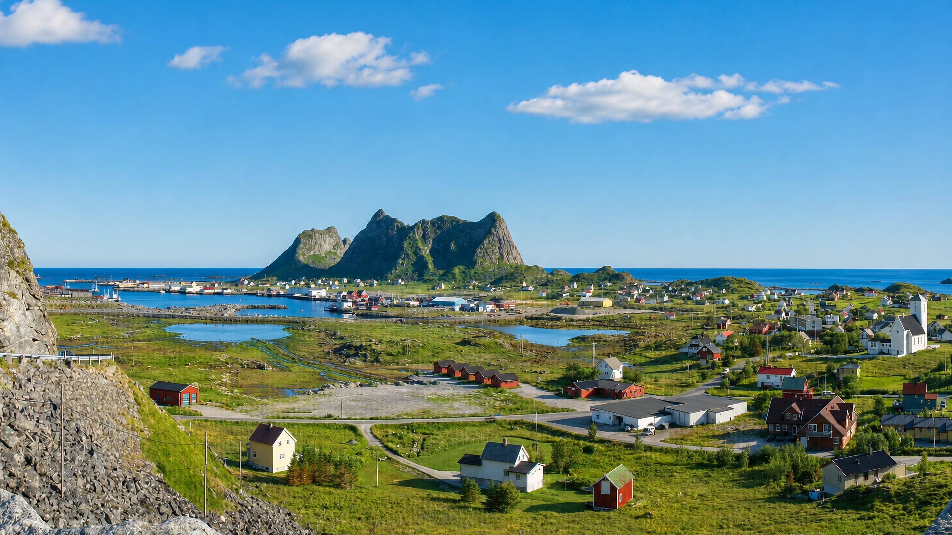Sorland village on Vaeroy, Norway, with houses and harbour below a jagged Lofoten peak beside the sea