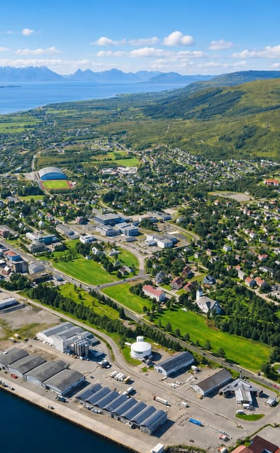 Aerial view of Sortland, Norway, along a coastal sound with harbour quays and green mountains across the water.
